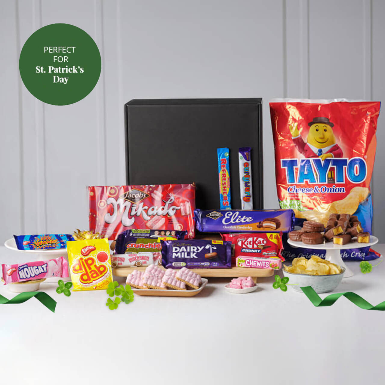 Irish Tastes of Home Treat Box featuring Tayto crisps, chocolate bars, sweets, biscuits, and snacks arranged around a black gift box